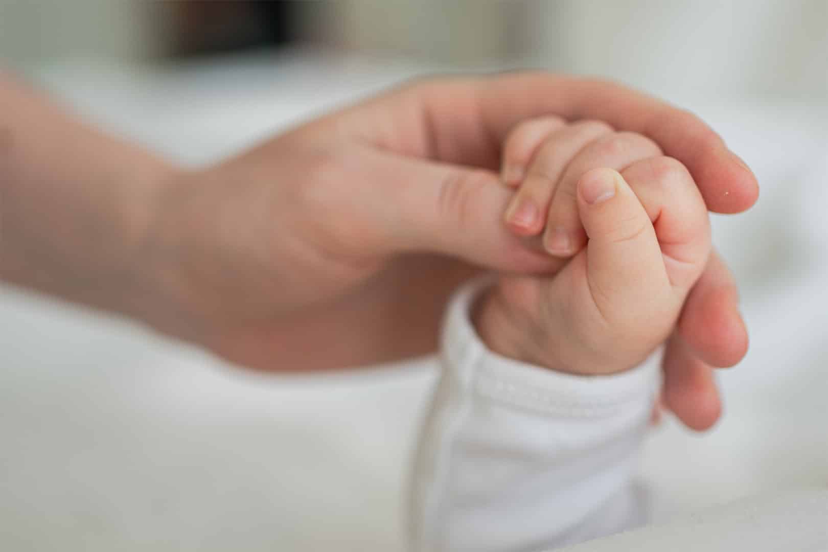 Erwachsene hält schützend die Hand eines Babys.