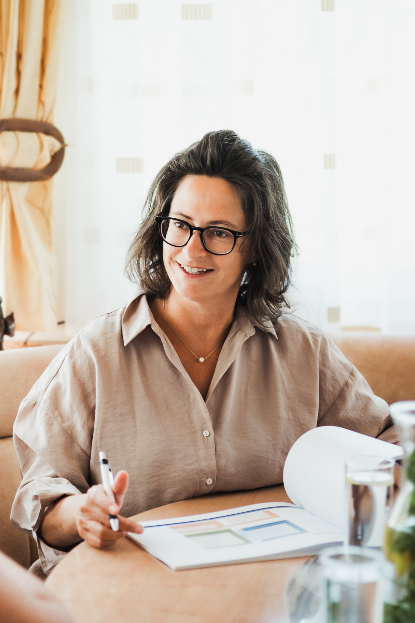 eraterin mit Brille sitzt an einem Tisch und erklärt einer älteren Frau anhand von Unterlagen ein Konzept in ruhiger Gesprächsatmosphäre.