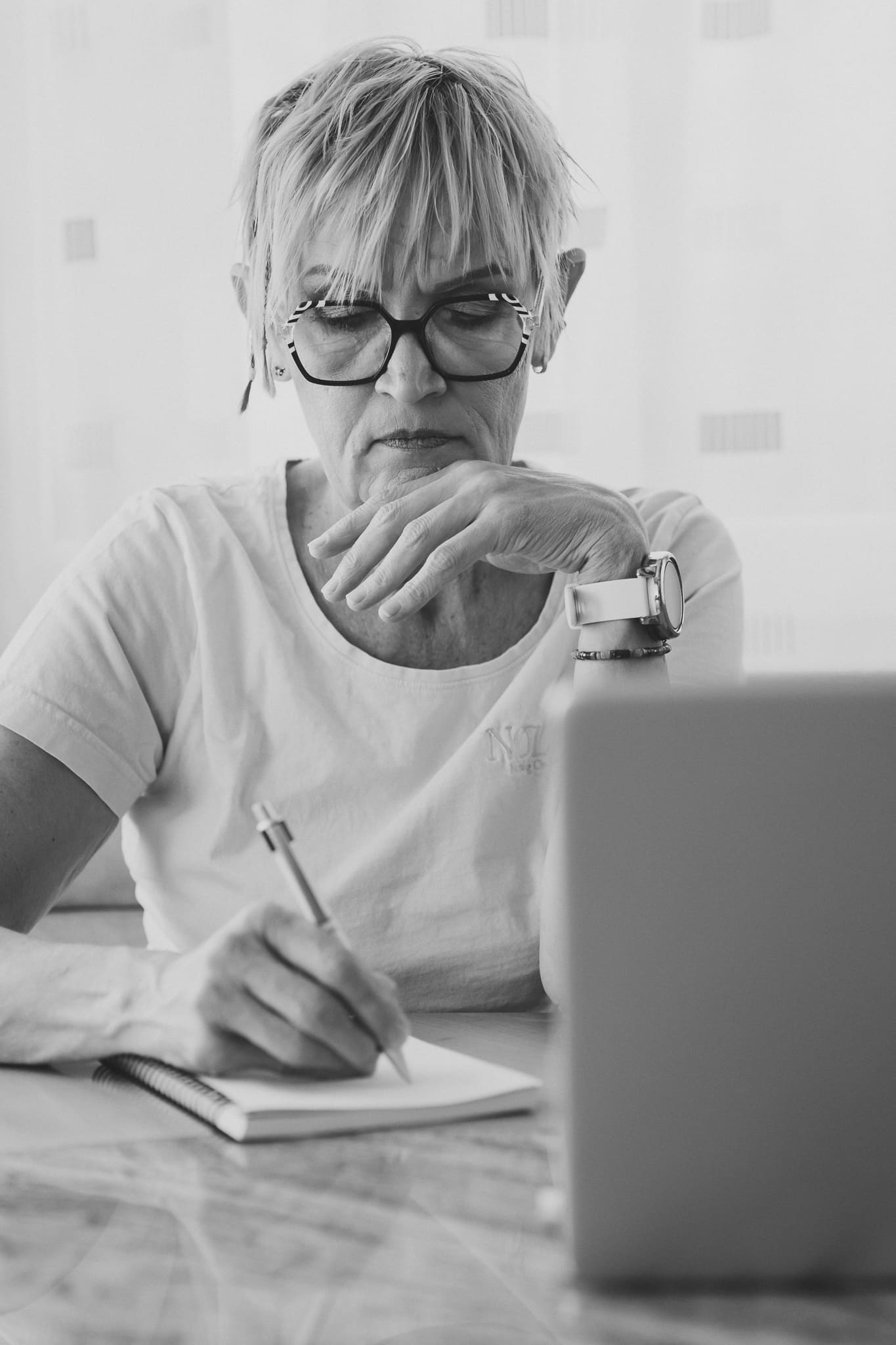 Pflegekraft dokumentiert Pflegeleistungen am Tisch mit Laptop.